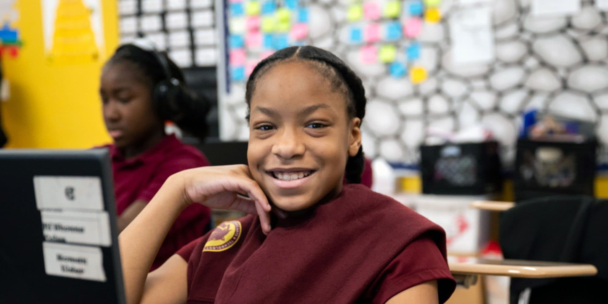Smiling student in a maroon CATA uniform at a desk beside a laptop.