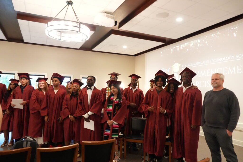 Young adults in graduation gowns and caps with an adult.