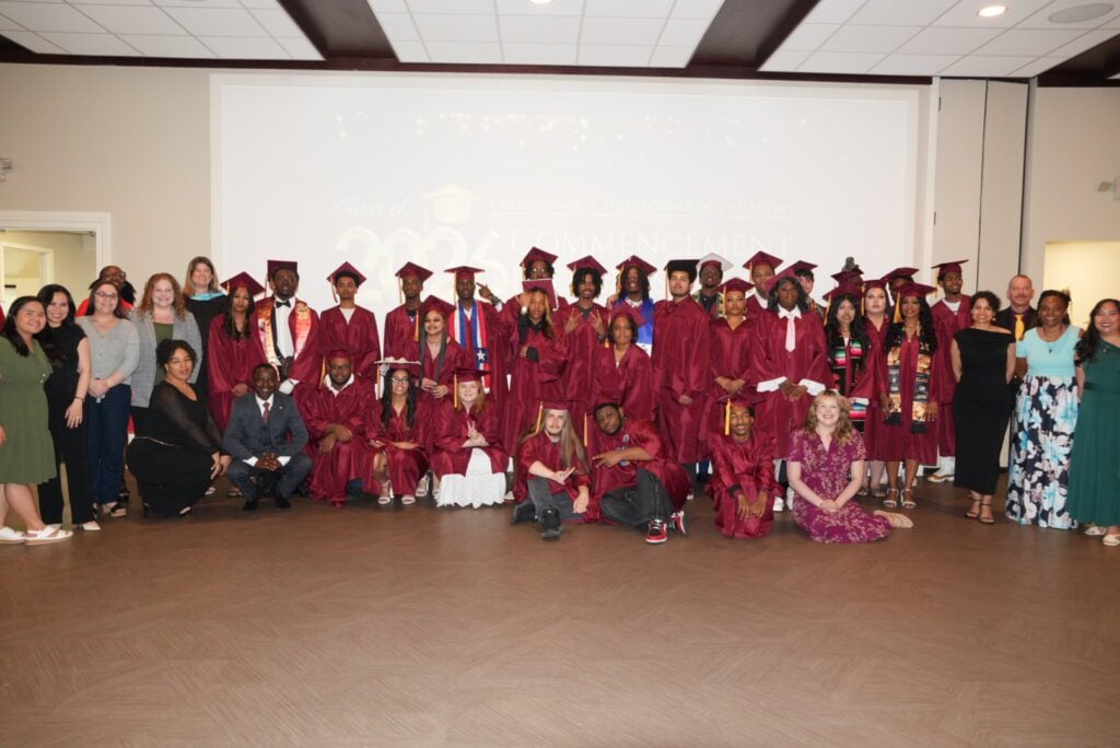 Group photo of graduates in maroon caps and gowns with adults.