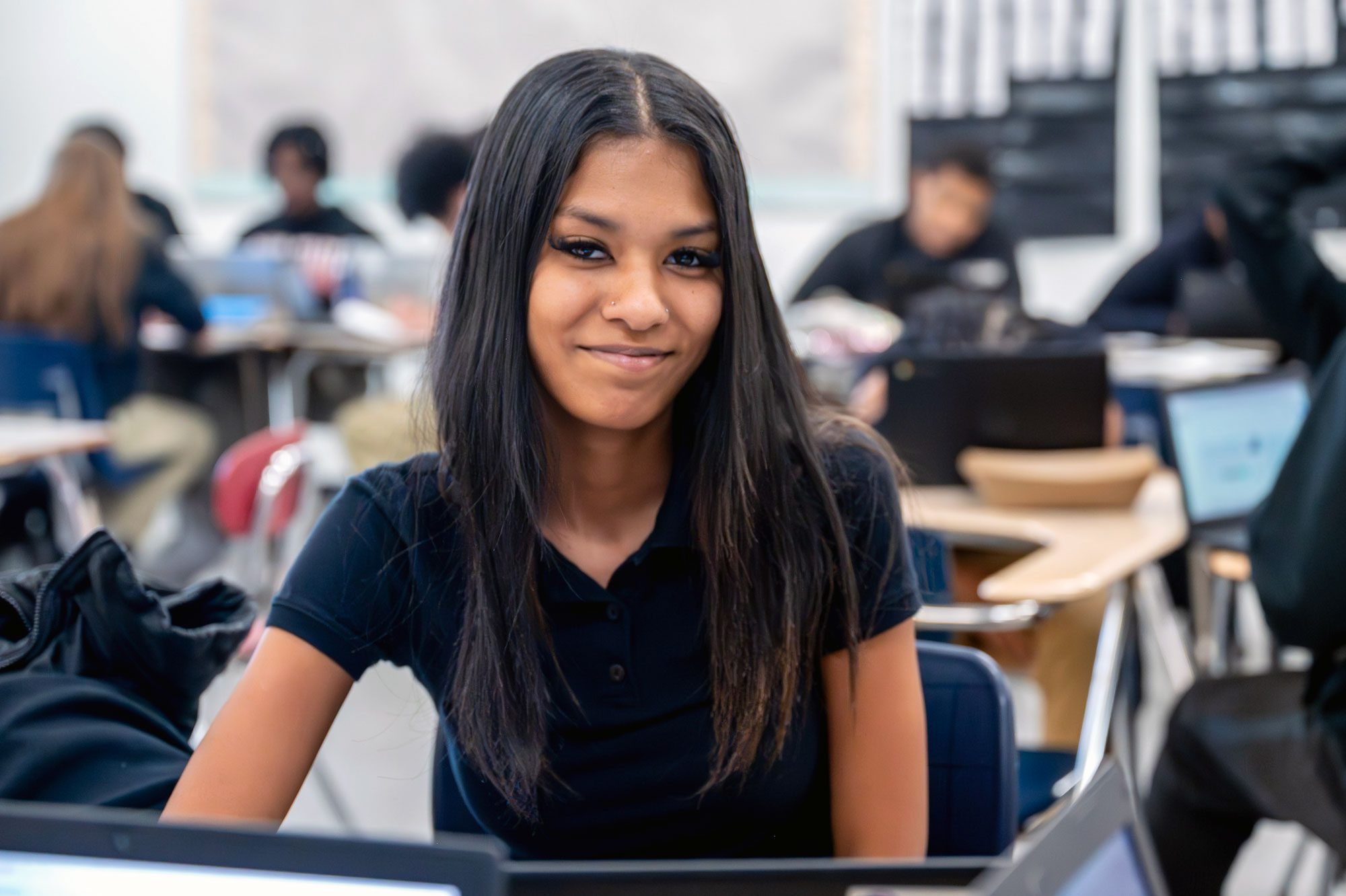 Smiling high school student seated at a desk in a classroom.