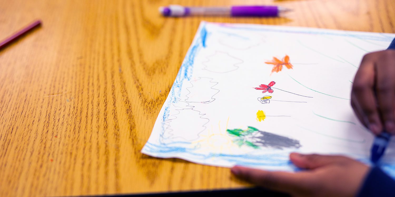 Student drawing and coloring a picture of flowers.